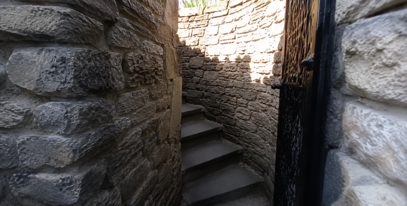 A tight corner outside with grey stone, looking through an archway towards curving stairs